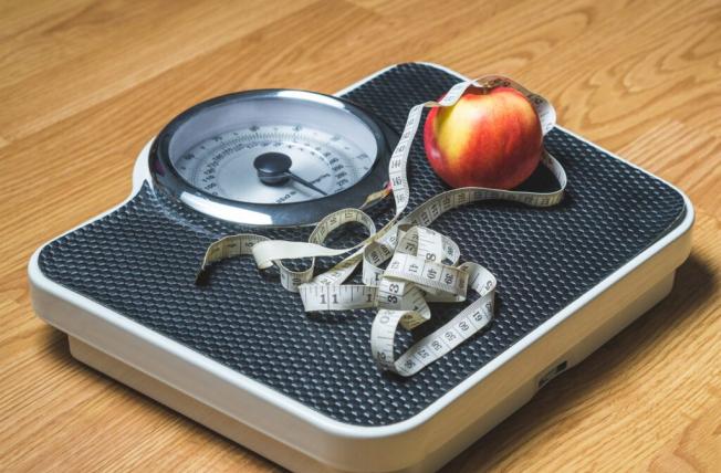 A scale with a tape measure and an apple on it