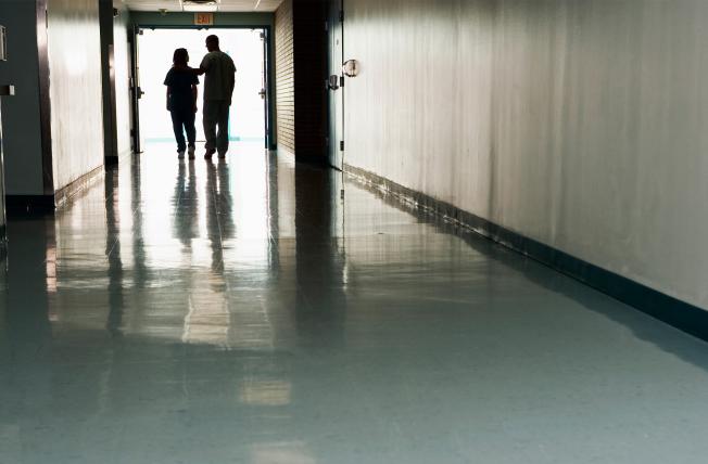 Two health care workers in a long hallway, one touching the other's shoulder