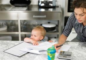 Mother with baby looking stressed while calculating bills
